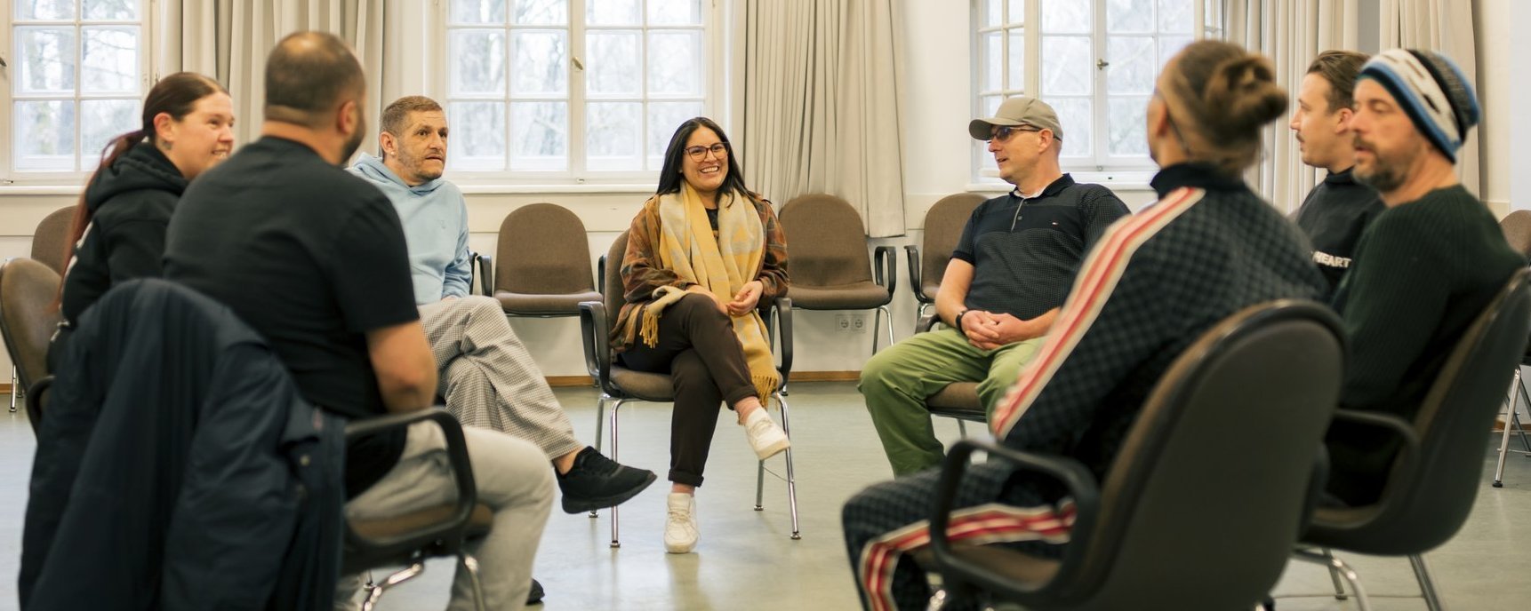 Acht Menschen sitzen in einem Stuhlkreis und unterhalten sich.