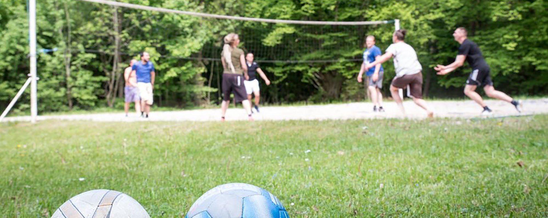 Nahaufnahme: zwei Volleybälle im Vordergrund - dahinter spielen eine Gruppe Männer am Netz