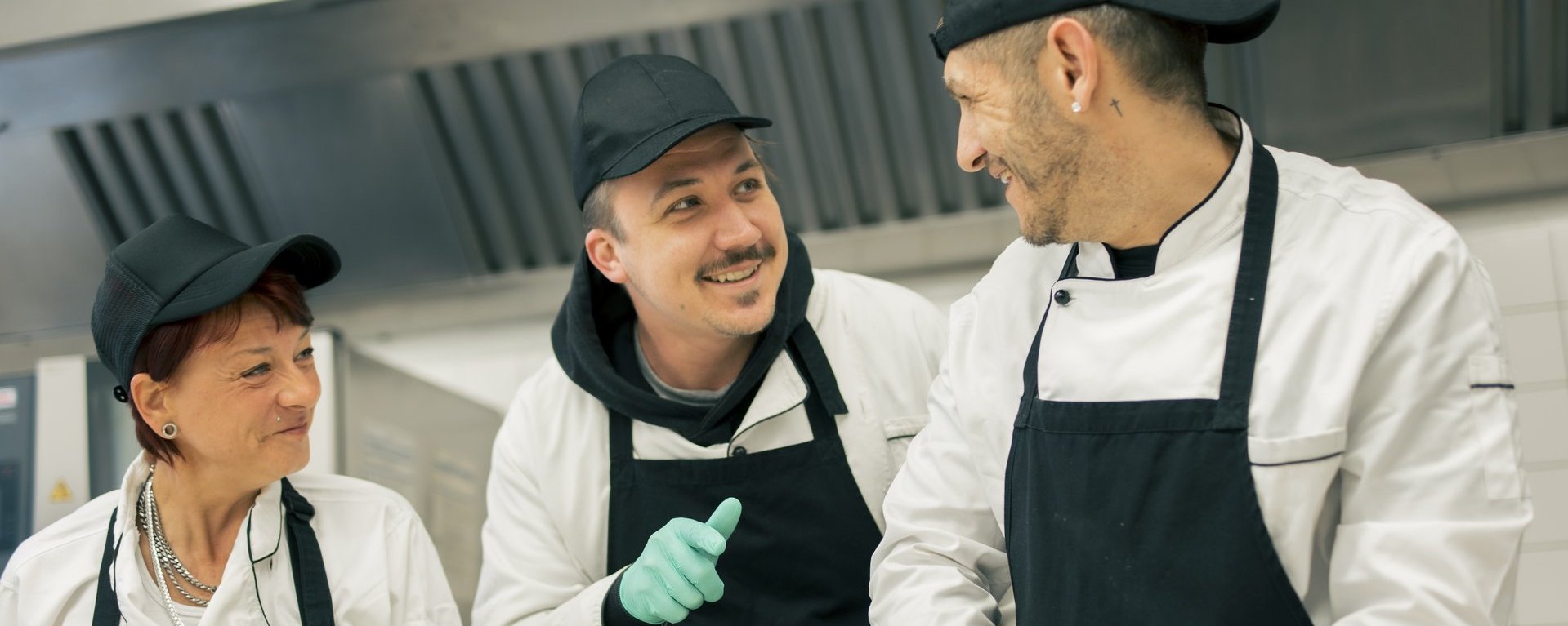Drei Personen arbeiten in der Küche und unterhalten sich lachend.