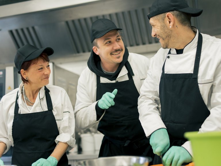 Drei Personen arbeiten in der Küche und unterhalten sich lachend.