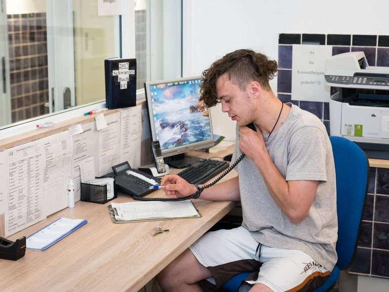 ein junger Mann im Büro - er telefoniert, hält einen Kugelschreiber in der Hand und blickt auf ein Blatt Papier 