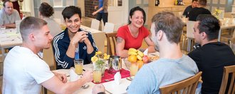 eine Gruppe Frauen und Männer sitzen im Speisesaal, warten auf das Essen und unterhalten sich - sehr fröhliche Stimmung