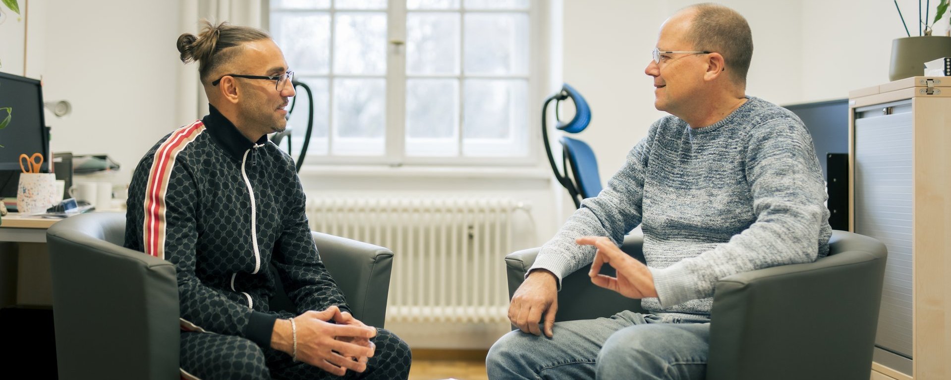 Zwei Männer sitzen in schwarzen Sesseln und unterhalten sich.
