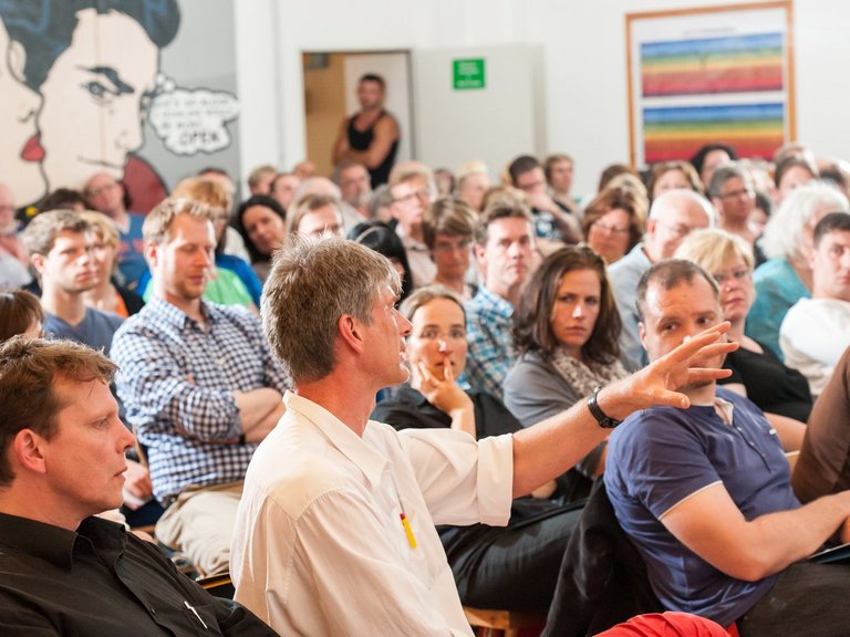 Vortrag im voll besetzten Saal: ein Mann aus dem Publikum spricht gerade